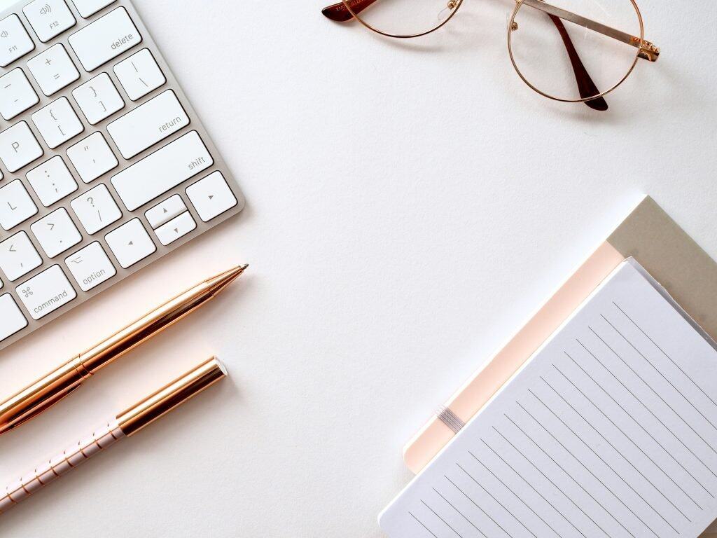 a keyboard, glasses, pen and notepad on a desk